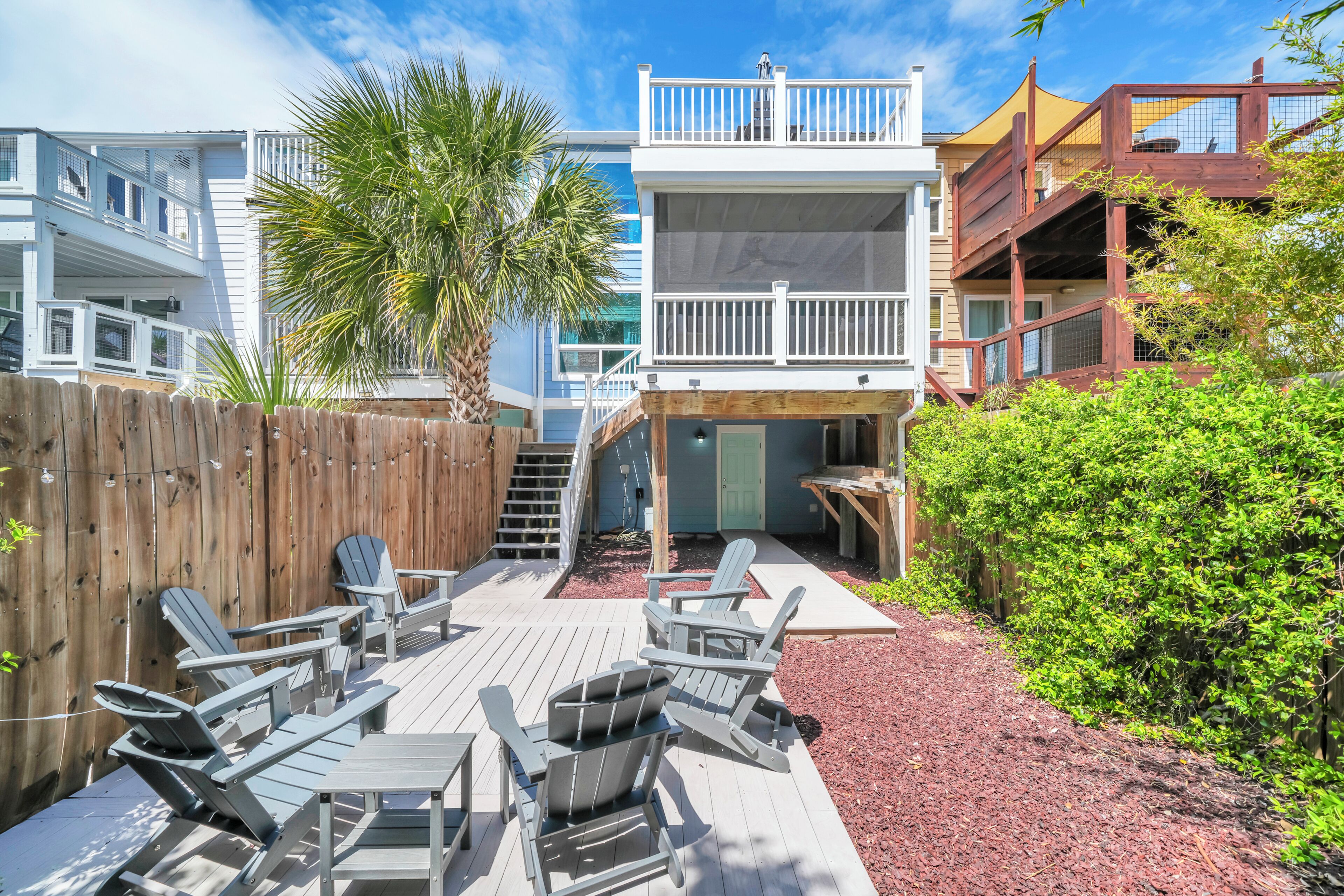 A deck with Adirondack chairs, a wooden fence, and a two-story building with a balcony.