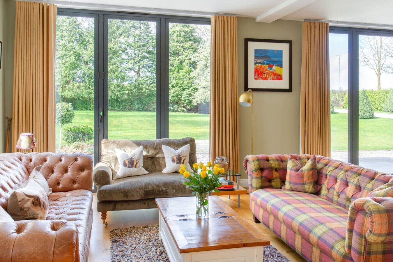 A spacious living room with large windows, a sofa set, a coffee table, and a framed picture on the wall.