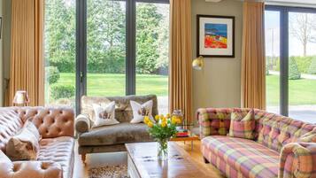A spacious living room with large windows, a sofa set, a coffee table, and a framed picture on the wall.