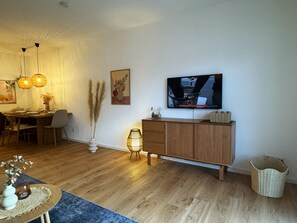 Un salon moderne avec une table à manger en bois, des chaises, un téléviseur fixé au mur et un meuble.