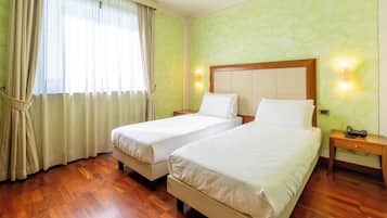 Habitación de hotel con dos camas, suelo de madera, paredes verdes y una ventana con cortinas.