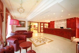 Una hall d'albergo con una reception, confortevoli posti a sedere, un pavimento decorato e un soffitto con motivi floreali.