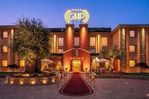 Ingresso di un hotel con tappeto rosso, insegna con 'GHP' e stelle, e facciata ben illuminata.