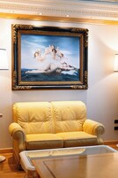 Una stanza con un quadro incorniciato, un divano giallo e un tavolo con piano in vetro.