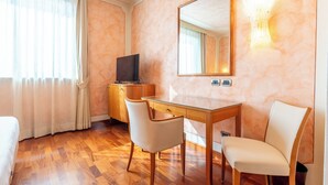 A hotel room with a wooden floor, a desk with two chairs, a television, a mirror, and a light fixture. - Grand Hotel del Parco (Stezzano)