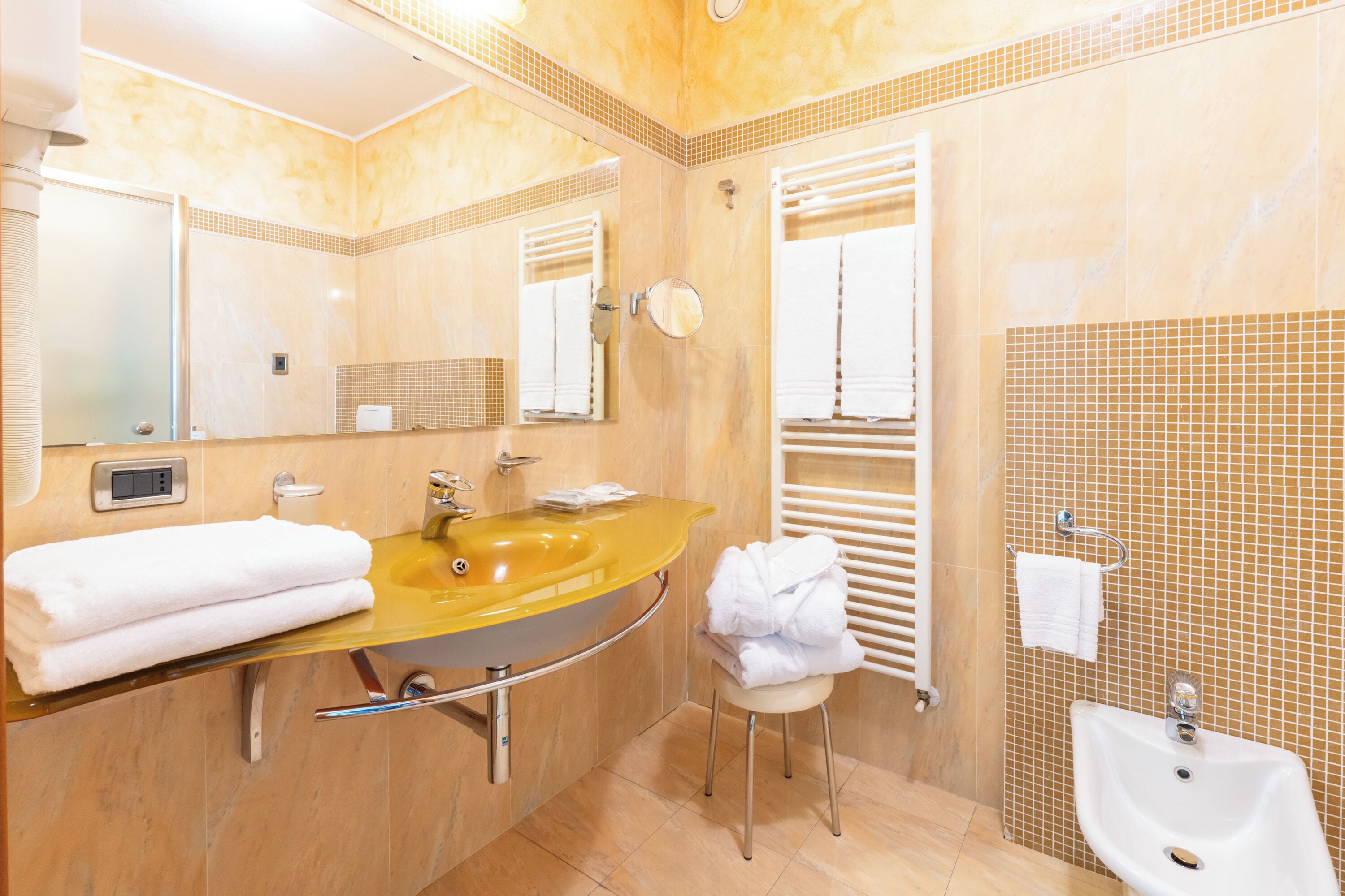 Ein Badezimmer mit einem gelben Waschbecken, einem Spiegel, einem weißen Handtuch und einer weißen Toilette.