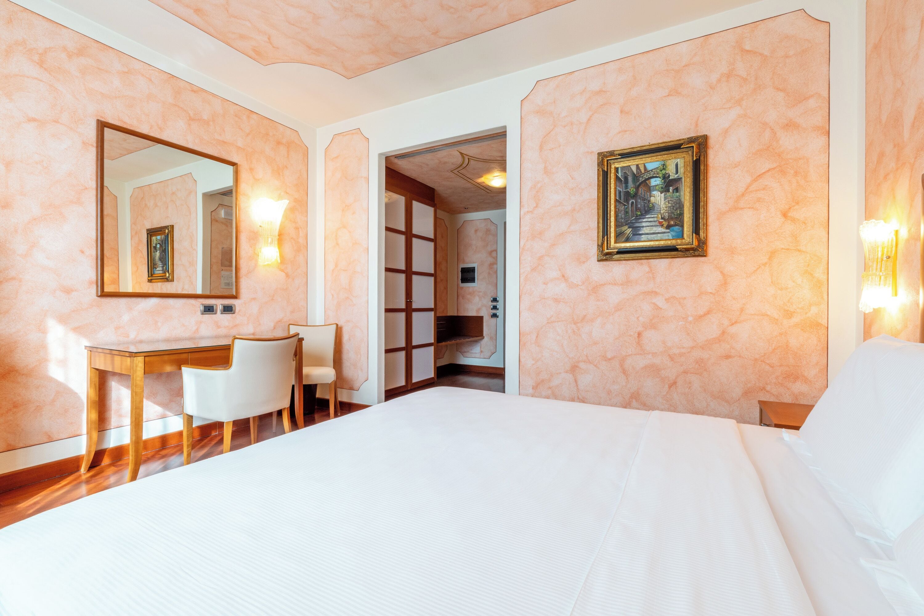 Habitación de hotel con una cama grande, un escritorio con silla, un espejo y un cuadro en la pared.