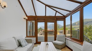 A sunroom with a wooden ceiling, large windows, a sofa, a table, and a view of the outdoors. - Loch View, Hot Tub, Near Loch Lomond, Pet-friendly (Arrochar)