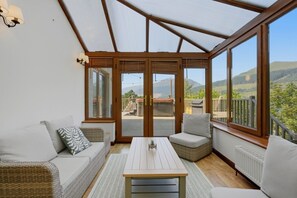 Ein Wintergarten mit Holzbalkendecke, großen Fenstern, einer Couch, einem Tisch und Blick ins Freie.
