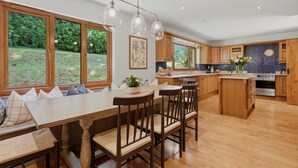 A modern kitchen with wooden cabinets, a central island, and large windows overlooking a garden. - Loch View, Hot Tub, Near Loch Lomond, Pet-friendly (Arrochar)