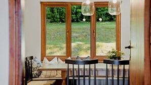 A dining area with a wooden table and chairs, a bench with cushions, and a view through large windows to a grassy outdoor area. - Loch View, Hot Tub, Near Loch Lomond, Pet-friendly (Arrochar)