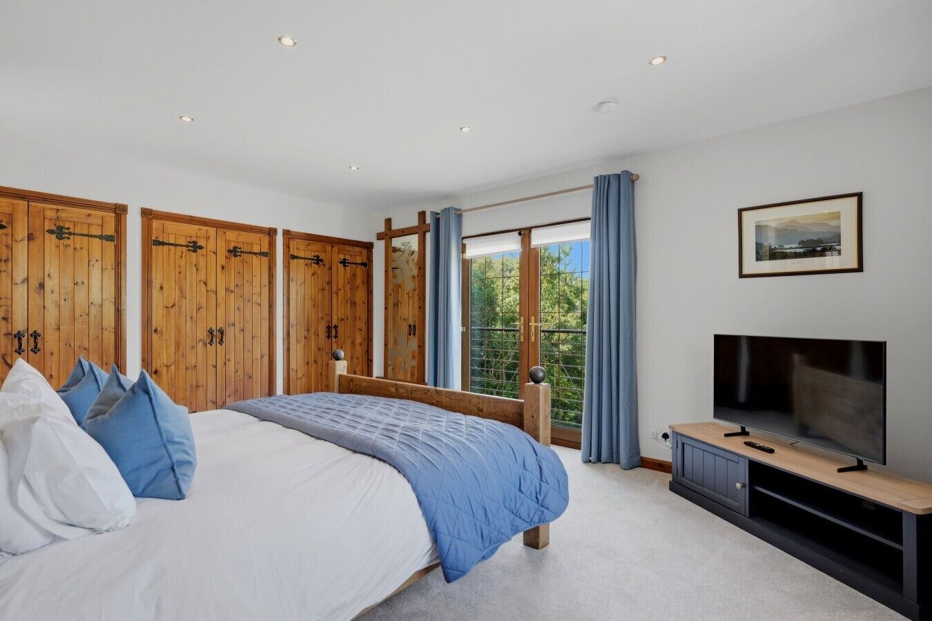 Een slaapkamer met een groot bed, een houten garderobe, een televisie en een raam met gordijnen.