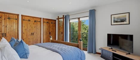 A bedroom with a large bed, wooden wardrobe, a TV, and a window with curtains.