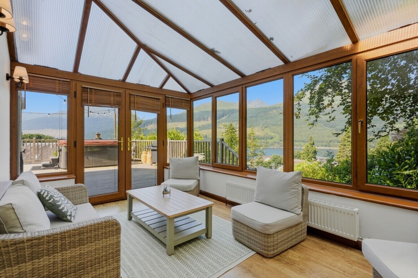 A sunroom with a view of a lake and mountains, furnished with a sofa, chairs, and a table.