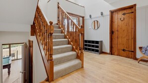 A staircase with wooden balusters leading to a landing, a wooden door with a circular mirror above it, and a view of the outdoors through a glass door. - Loch View, Hot Tub, Near Loch Lomond, Pet-friendly (Arrochar)