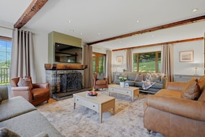 Ein geräumiges Wohnzimmer mit Kamin, Ledersofas und einem großen Fenster mit Blick ins Freie.