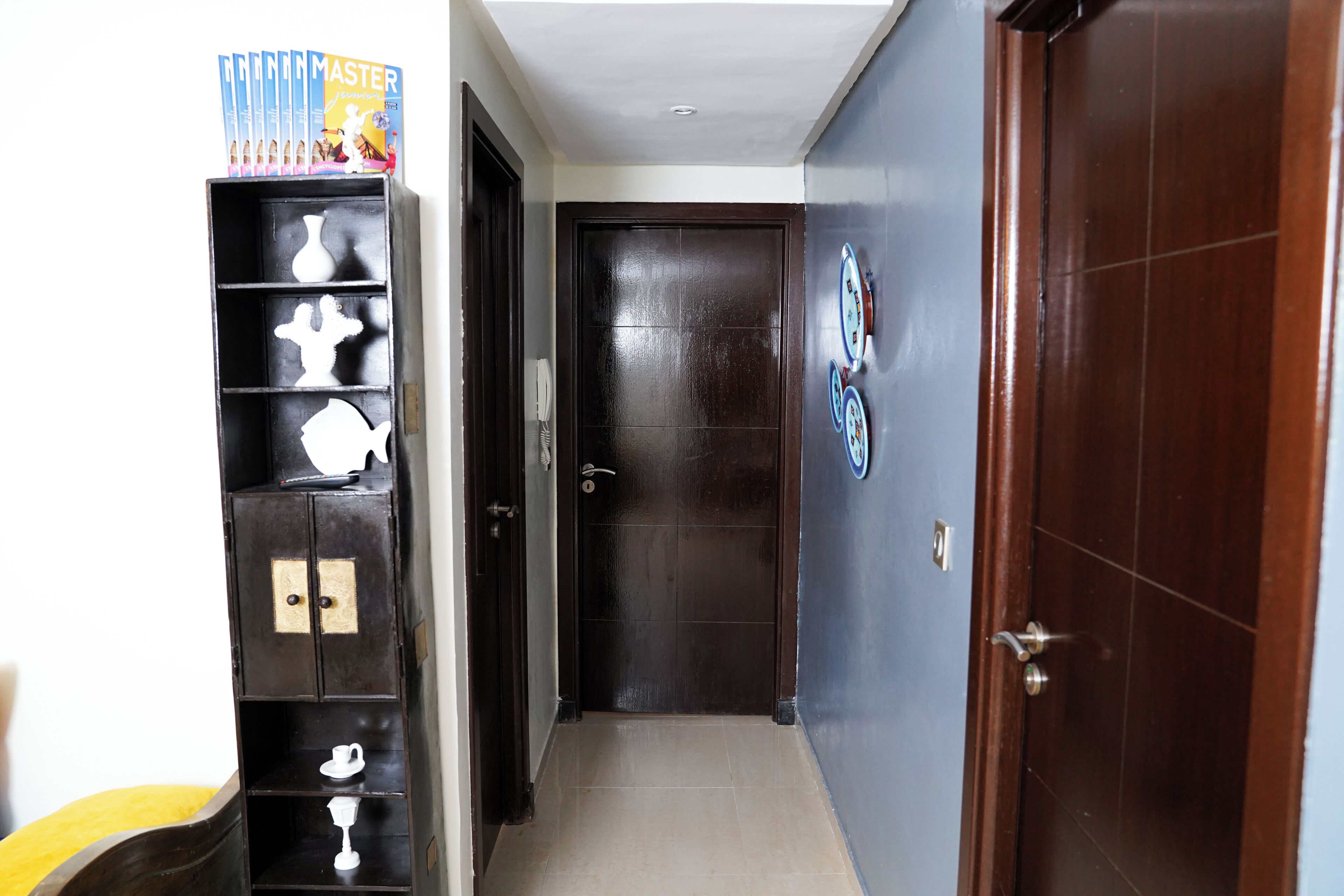 A hallway with a dark wooden door, a wall-mounted clock, and a shelf with decorative items.
