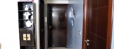 A hallway with a dark wooden door, a wall-mounted clock, and a shelf with decorative items.