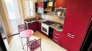 A kitchen with red cabinets, a gas stove, a sink, and a dining area with a table and chairs. - Chic Designer Apartment with Pool Access (Agadir)