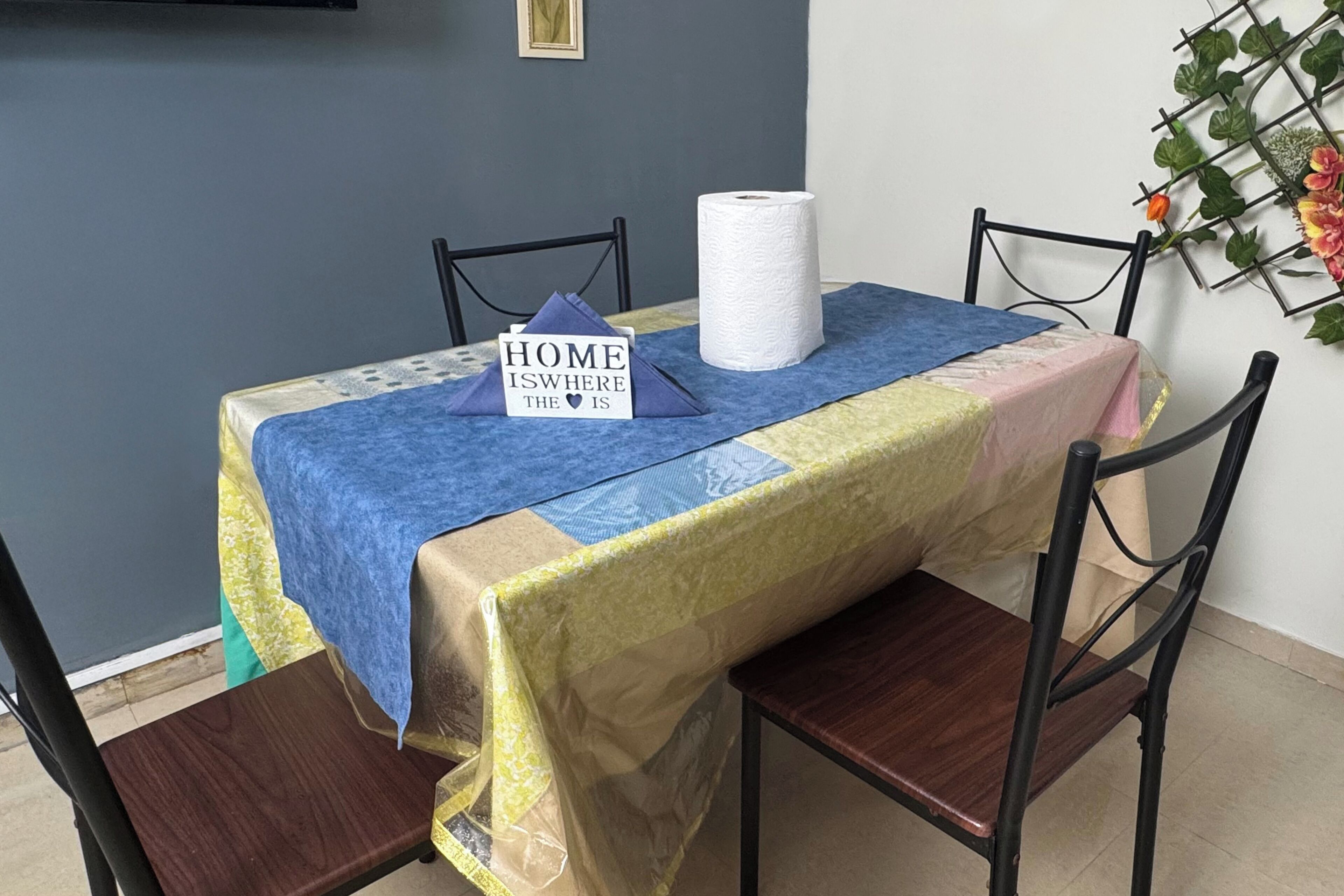Una mesa de comedor con mantel azul y amarillo, un rollo de toallas de papel y un letrero que dice 'HOME IS WHERE THE ♥ IS'.