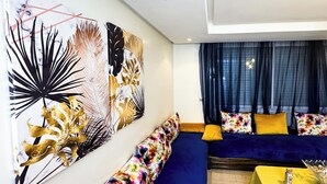 A modern living room with a blue sofa, yellow cushions, and a large abstract painting on the wall. - Chic Designer Apartment with Pool Access (Agadir)