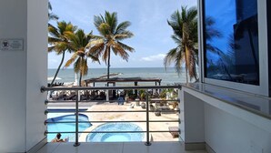 A balcony with a view of a beach, palm trees, and a pool area. - Hotel Portoalegre (Coveñas)