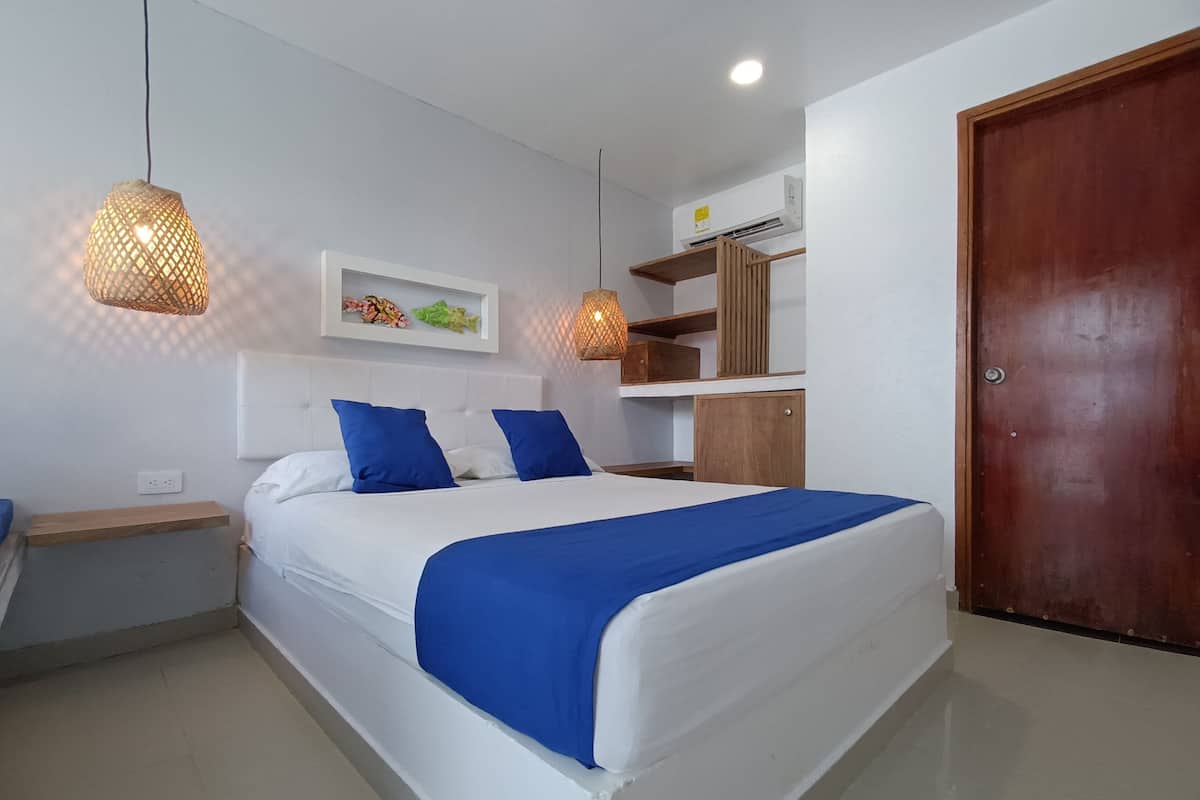 A bedroom with a bed, bedside tables, a wardrobe, a wall-mounted air conditioner, and a door.