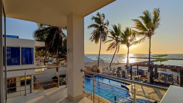 A balcony with a pool and a view of the sunset over the ocean, palm trees, and a lounge area. - Hotel Portoalegre (Coveñas)