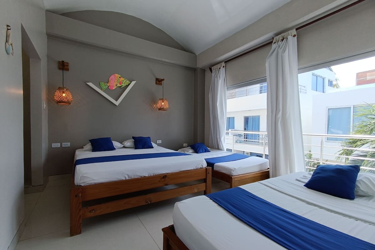A hotel room with two beds, a balcony with a railing, and a view of buildings outside.