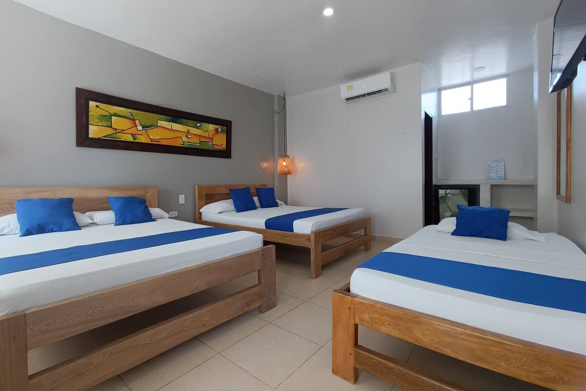 A hotel room with two wooden beds, a painting on the wall, an air conditioning unit, and a window.