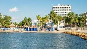 A beachside hotel with a pool, palm trees, and a building in the background. - Hotel Portoalegre (Coveñas)