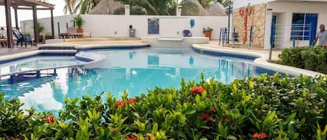 Une piscine entourée d’une terrasse, de palmiers et d’un bâtiment doté d’une porte bleue.