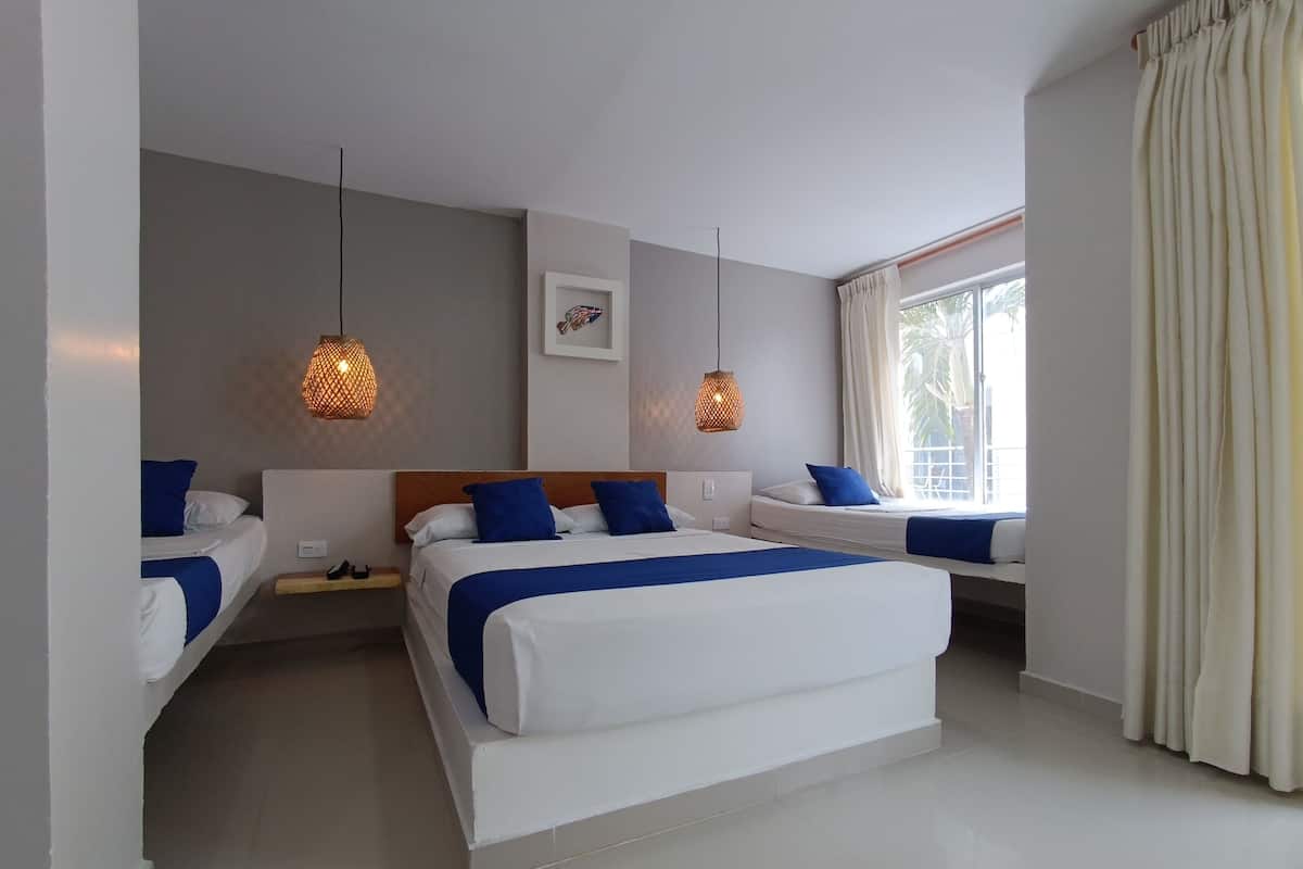 A hotel room with a large bed, bedside tables, hanging lamps, a window with curtains, and a framed picture on the wall.