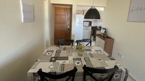 Un coin repas avec une table recouverte d’une nappe patchwork, deux chaises, une suspension et une porte donnant sur la cuisine.