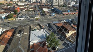 Une vue sur un paysage urbain à travers une clôture en treillis métallique, avec des bâtiments, des routes et un ciel dégagé.