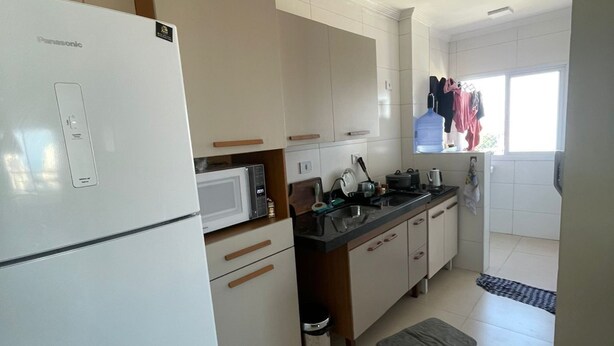 Une cuisine avec un réfrigérateur blanc, un four à micro-ondes et une cuisinière, des armoires en bois, un évier et une fenêtre où du linge est étendu pour sécher.