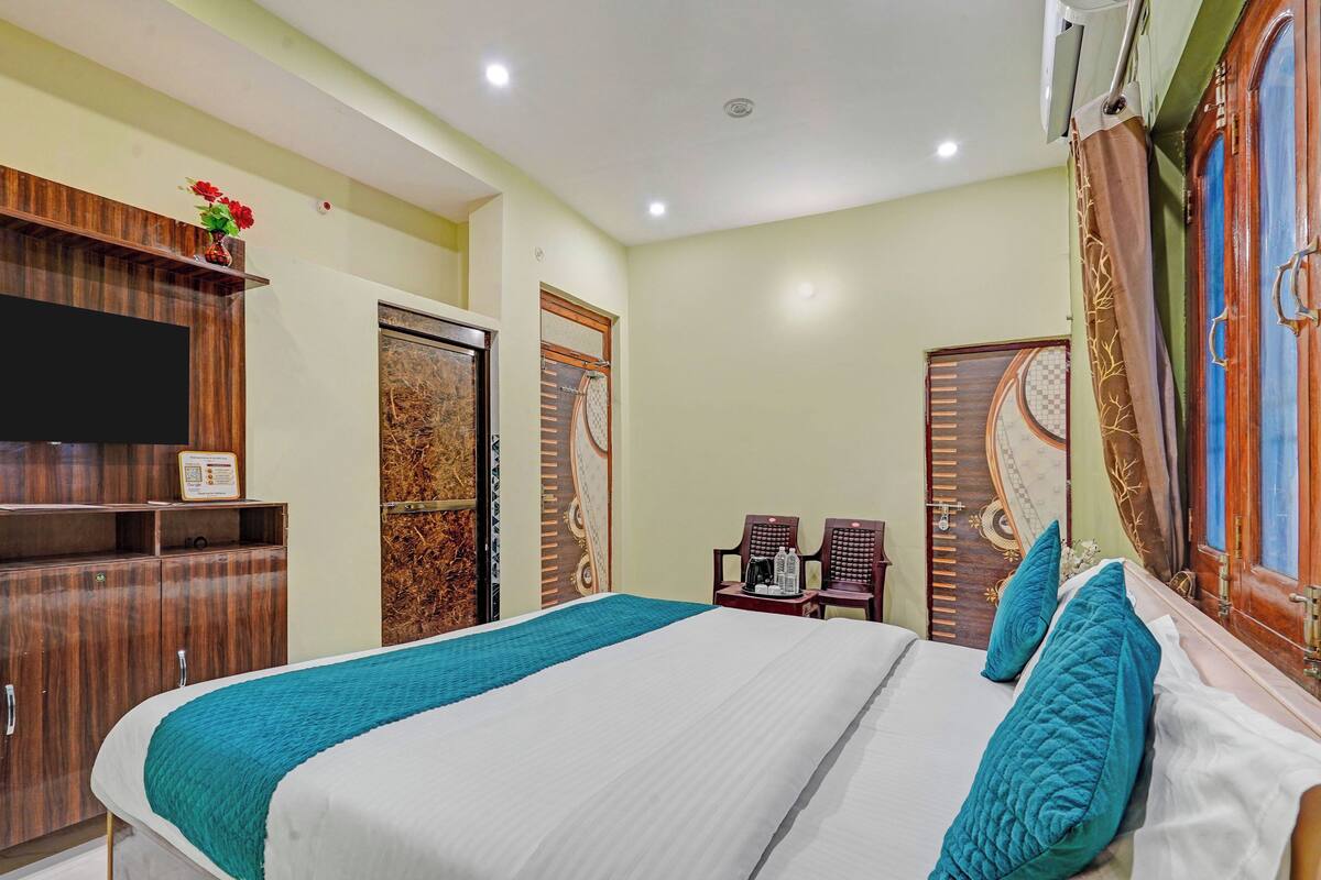 A hotel room with a large bed, wooden wardrobe, two chairs, a television, and a decorative wall.