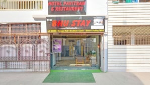 Un hotel llamado 'Bhu Stay' con un letrero que enumera servicios como habitaciones con aire acondicionado, salón de banquetes, desayuno, almuerzo, cena, estacionamiento y Wi-Fi.
