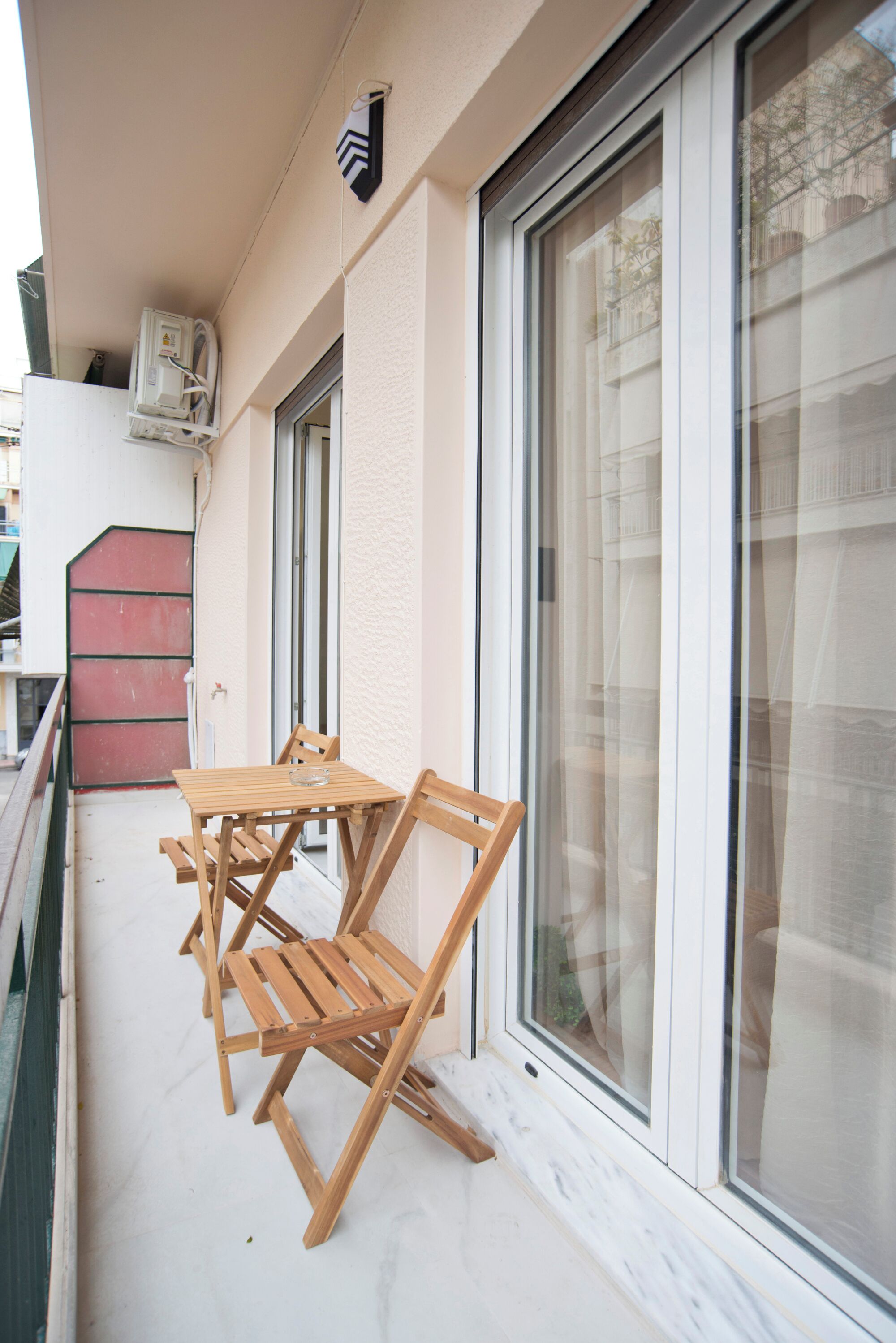 A balcony with a table and chairs, a sliding glass door, and a small air conditioning unit.