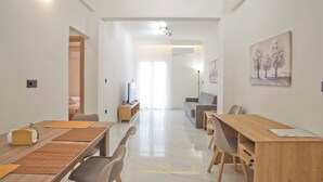 A modern living room with a sofa, a dining table with chairs, a TV, and a painting on the wall. - Athenian Glow Fully Renovated Apartment (Athina)