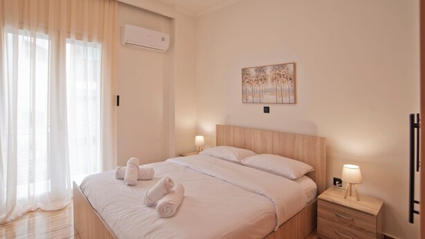 A hotel room with a bed, two bedside tables, a wall-mounted air conditioner, and a painting. - Athenian Glow Fully Renovated Apartment (Athina)