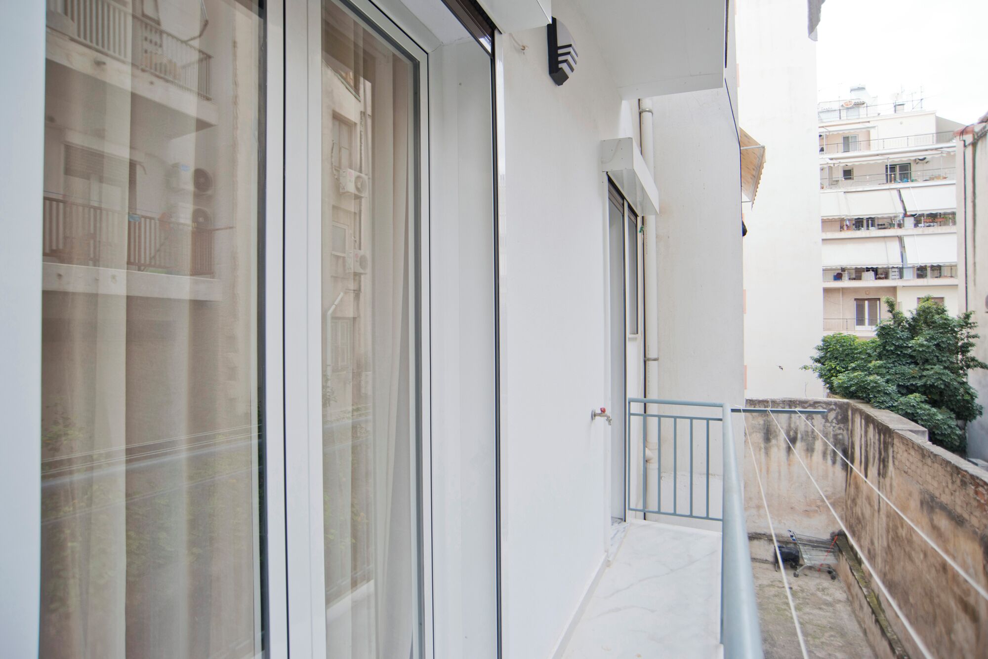 A balcony with a glass door, a metal railing, and a view of neighboring buildings.