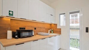 A modern kitchen with white cabinets, a wooden countertop, a microwave, a kettle, and a first aid sign. - Athenian Glow Fully Renovated Apartment (Athina)