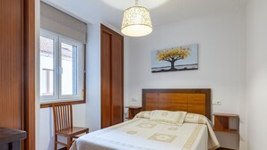 Une chambre à coucher avec un lit, une chaise, une table de chevet, une lampe et un tableau au mur.