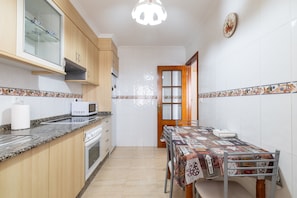A compact kitchen with a microwave, oven, and a dining table with a patterned tablecloth. - Río do Con Apartment with Free Private Parking in Vilagarcía de Arousa (Vilagarcía de Arousa)