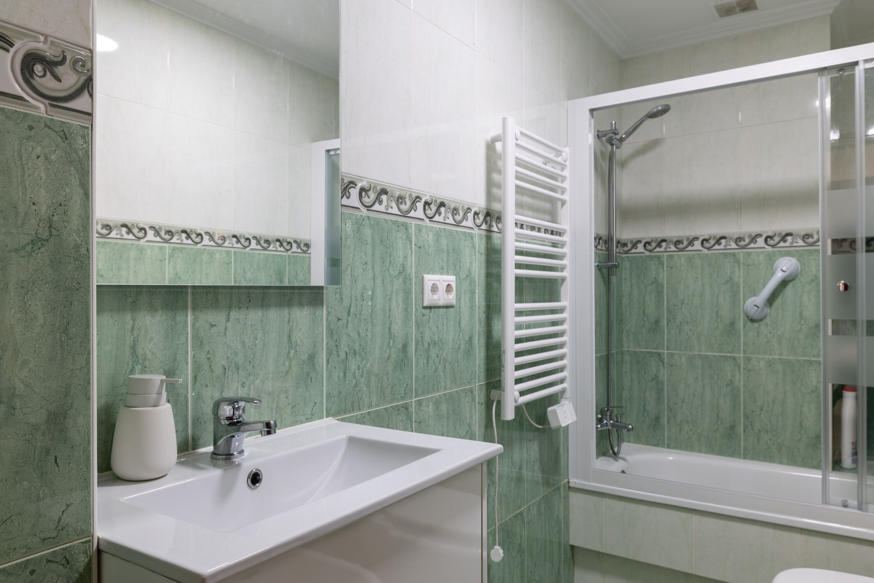 Ein Badezimmer mit Waschbecken, Spiegel, Dusche und Handtuchhalter.