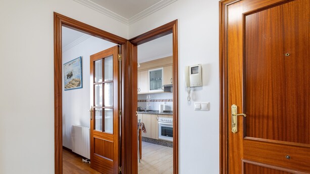 Un couloir avec des portes en bois menant à une cuisine équipée de placards et d’un four à micro-ondes.