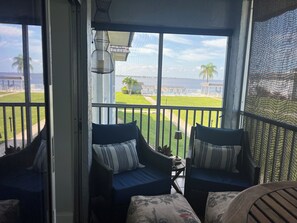 Ein Balkon mit Korbstühlen, einem kleinen Tisch und Blick auf einen Pool und Palmen.