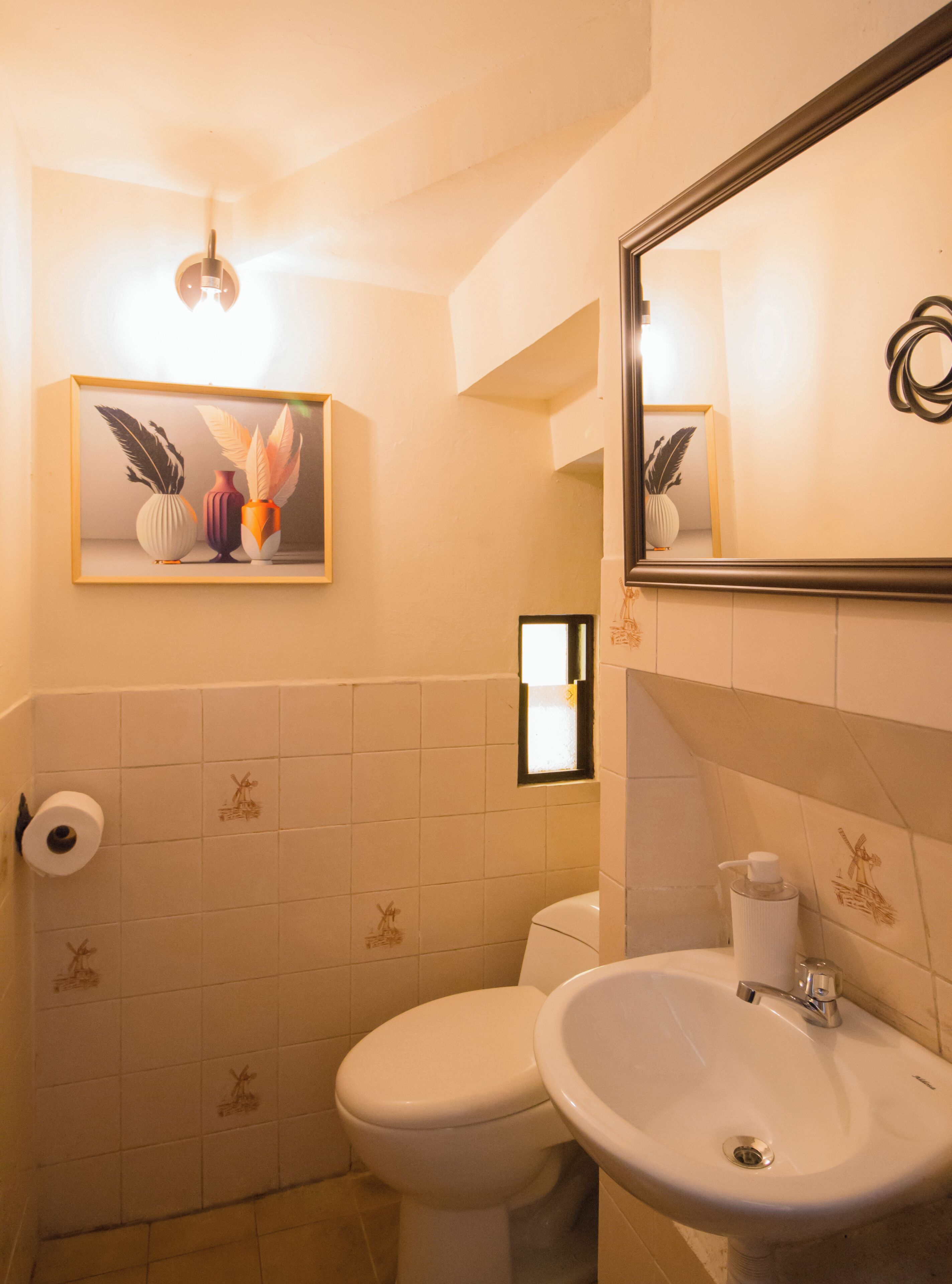 A bathroom with a toilet, sink, and a framed artwork above the sink.