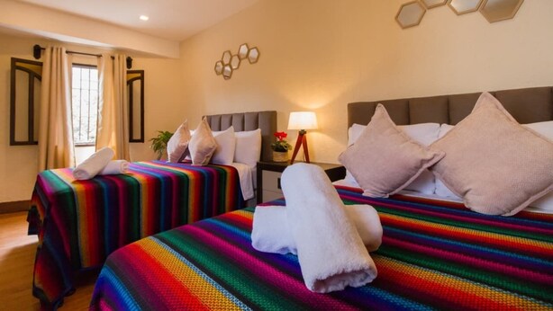 A hotel room with two beds, a ceiling fan, a wall-mounted light fixture, and a window with curtains. -  Casa Cami Anturi (Antigua Guatemala)